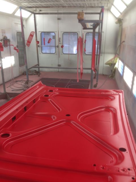 1964 Ford Fairlane - Underside of a freshly painted red car hood inside a professional paint booth.