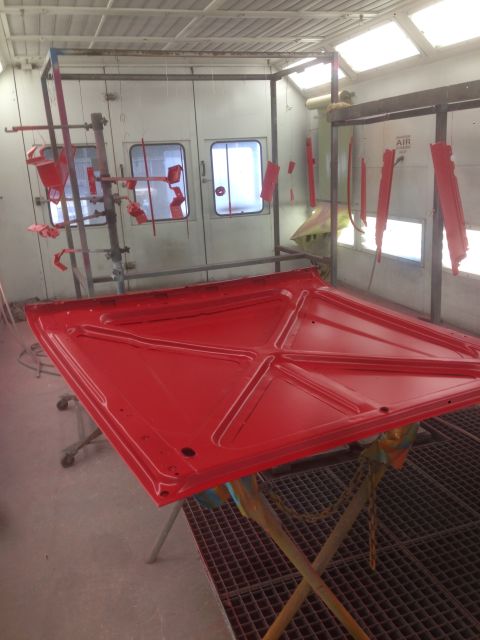 1964 Ford Fairlane - A red car hood is being painted in a professional paint booth.