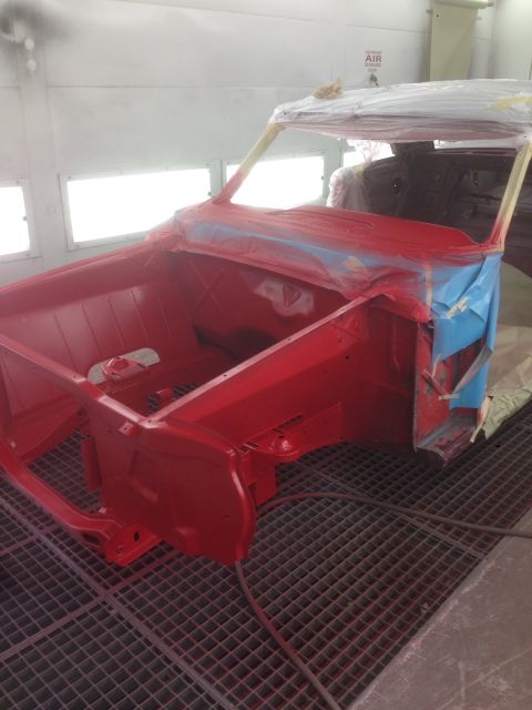 1964 Ford Fairlane - A car body is being prepped and painted red inside a professional spray booth.