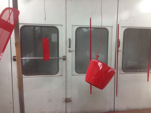 1964 Ford Fairlane - Several red car parts are suspended and drying inside a white paint booth.