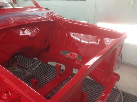 1964 Ford Fairlane - The red painted chassis of a car is visible in a paint booth, with the front section and engine bay area exposed.