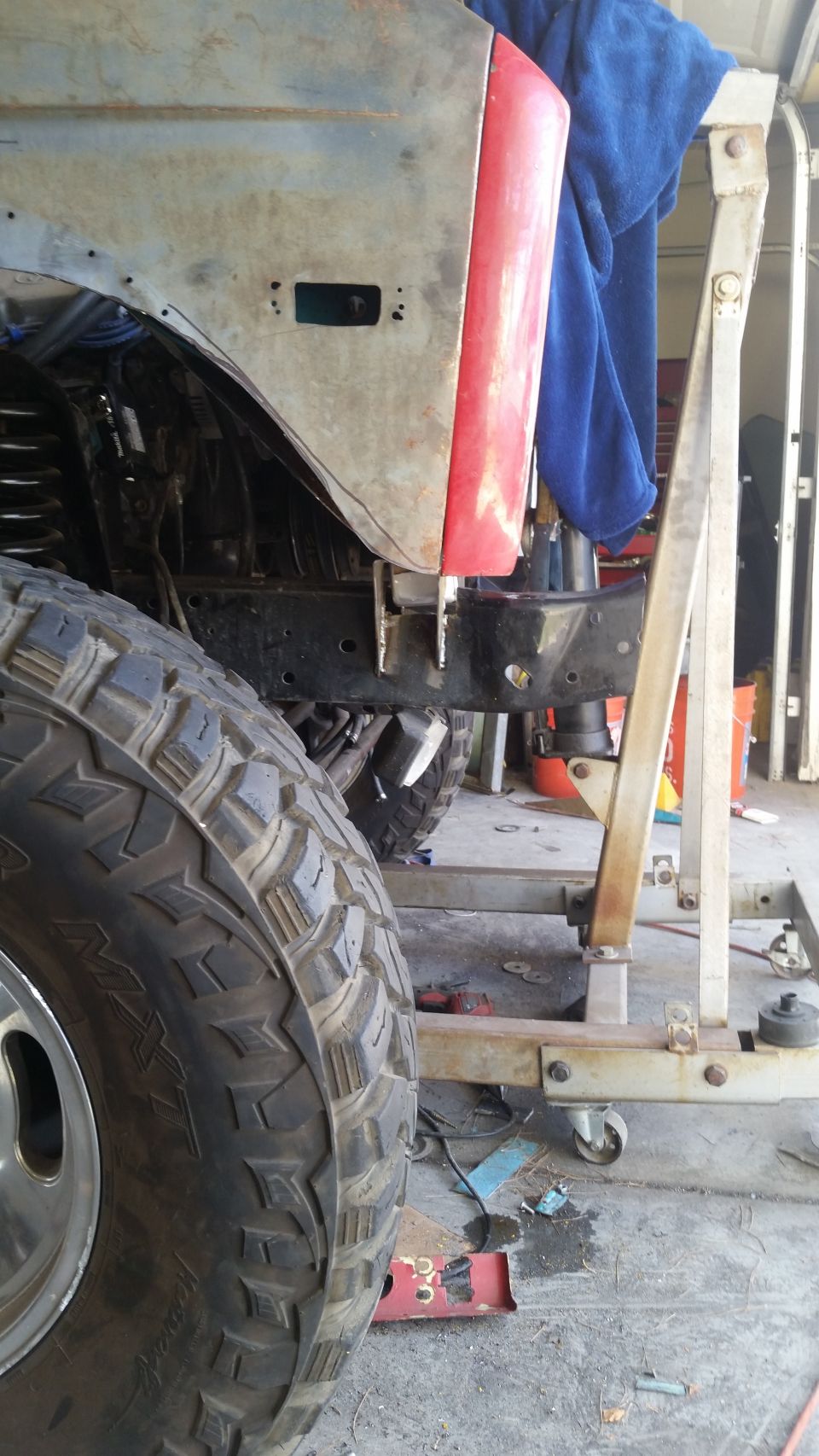 Close-up of a vehicle's fender and tire, possibly undergoing repair. A blue towel is draped over part of the bodywork