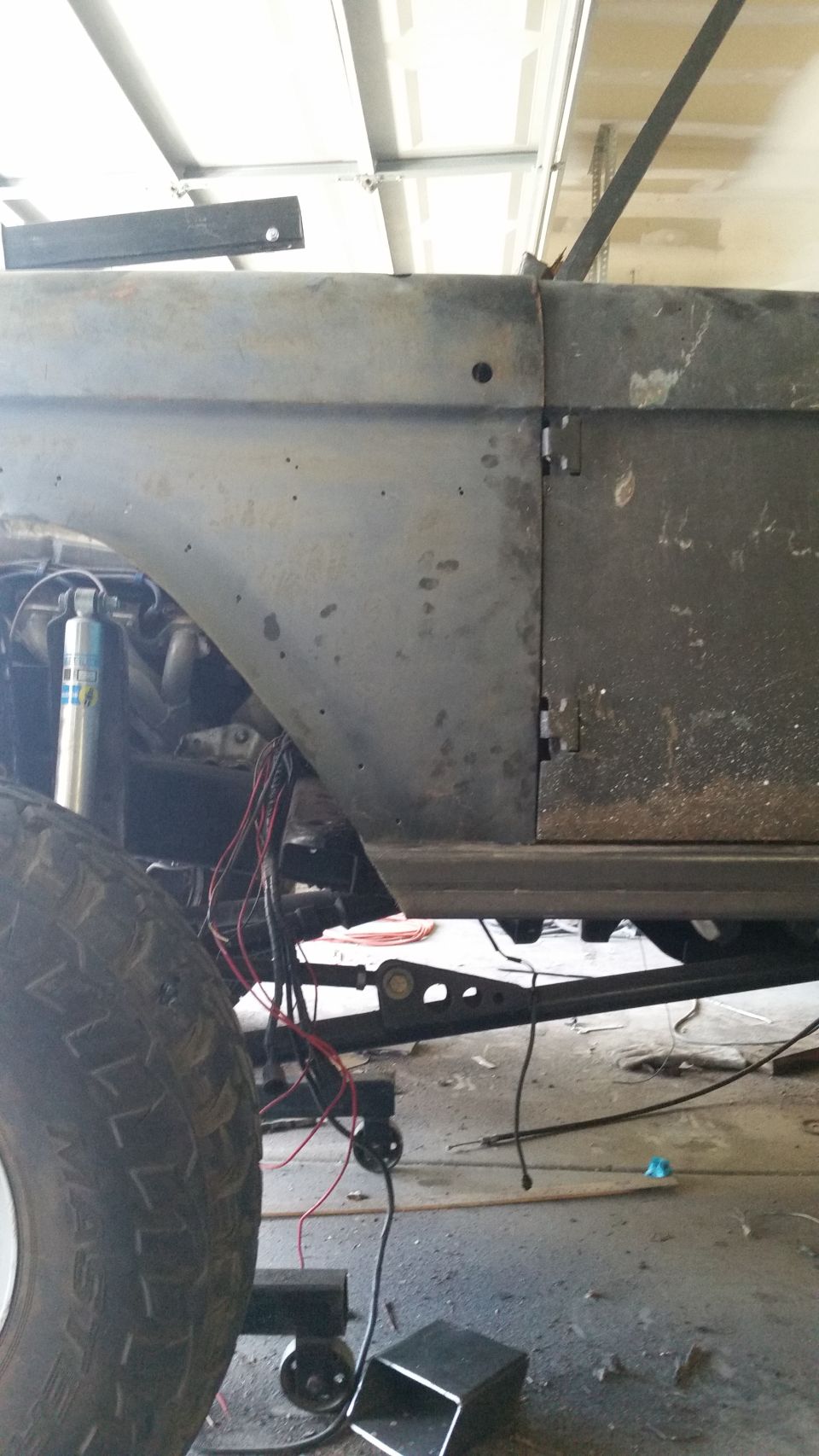 Side view of unfinished vehicle body with exposed wiring and suspension components