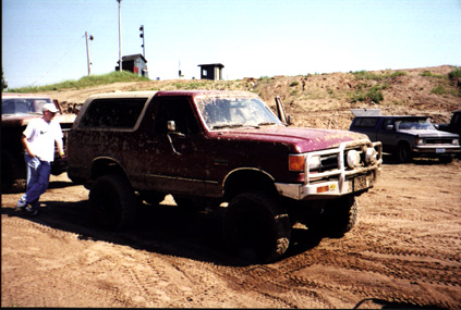 1991 Ford Bronco - Muddy 1991 Ford Bronco with off-road modifications parked on dirt, with another vehicle in the background.