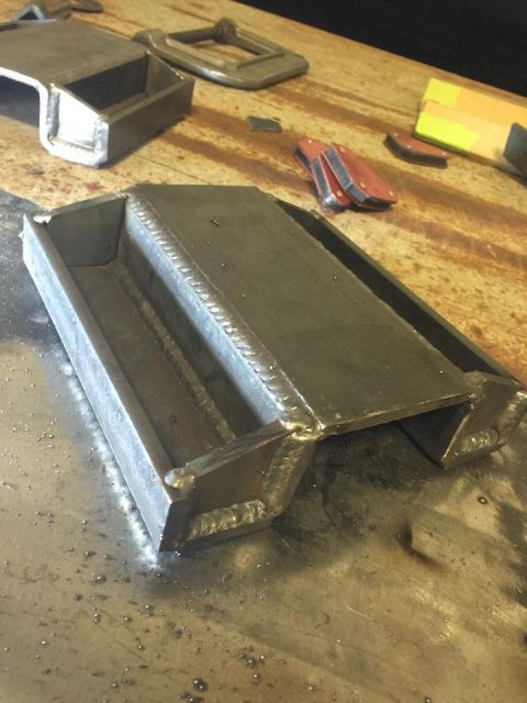 1979 Ford Bronco - A custom-fabricated metal component, likely for automotive use, sits on a workbench alongside tools and clamps. The Supermotors.net logo is…
