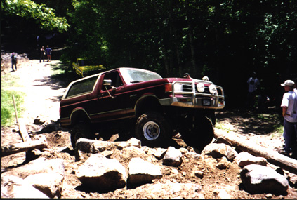 1991 Ford Bronco - A maroon Ford Bronco tackles a challenging off-road trail with onlookers present.