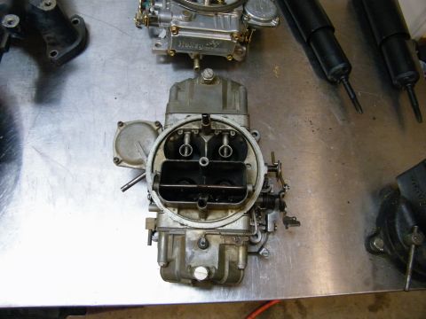 1967 Mercury Cougar - A close-up view of a carburetor, possibly a Holley model, resting on a metal surface alongside other engine parts.