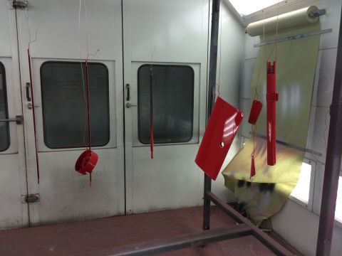 1964 Ford Fairlane - Various red car parts are suspended and drying inside a professional spray booth.