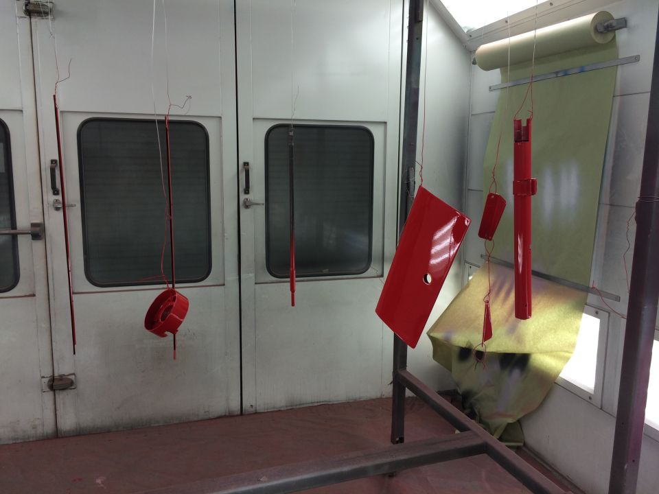 Red car parts hanging in a spray booth, ready for finishing