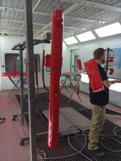 1964 Ford Fairlane - A man stands in a paint booth with various red car parts hanging to dry.