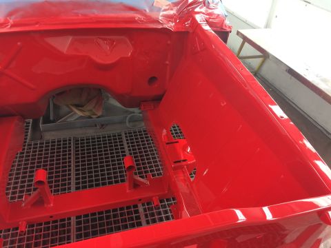1964 Ford Fairlane - Car body interior freshly painted red, resting on a metal grate.