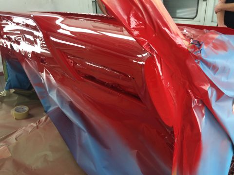1964 Ford Fairlane - A red car body panel is being painted, covered in protective sheeting and tape.