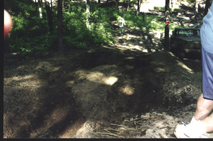 1991 Ford Bronco - A vehicle is parked on a dirt trail in a wooded area, with a person's legs visible in the foreground.