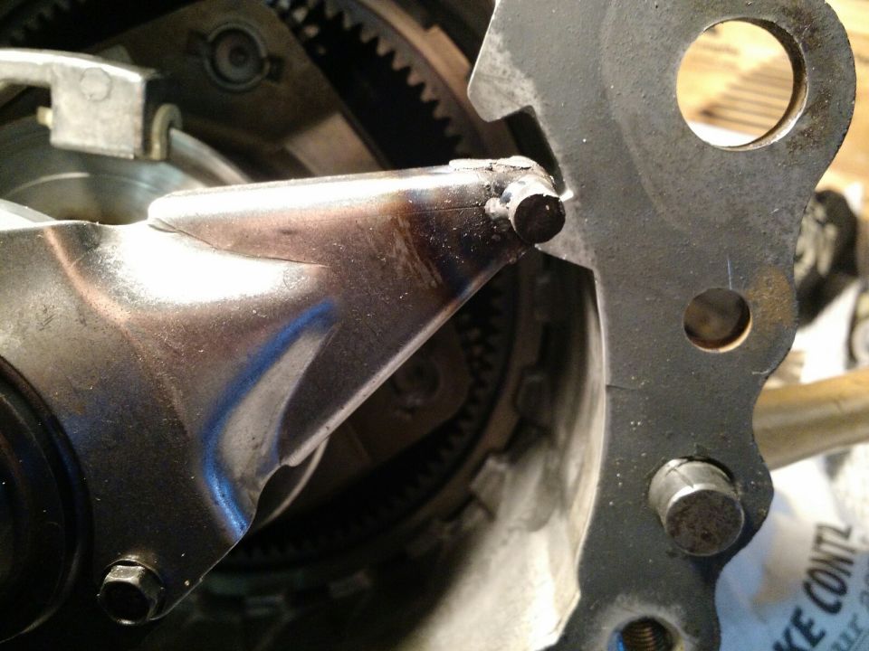 Close-up of a transfer case linkage mechanism with gears visible in the background. A metal lever connects to a pivot point