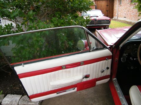 1968 Mercury Cougar - The interior of a 1968 Mercury Cougar shows off its white and red door panel, with another Cougar visible in the background.