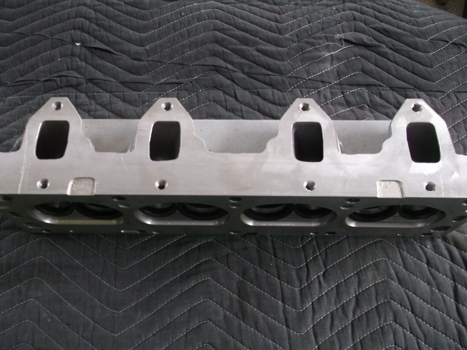 Engine cylinder head with four intake ports visible, resting on a quilted black surface