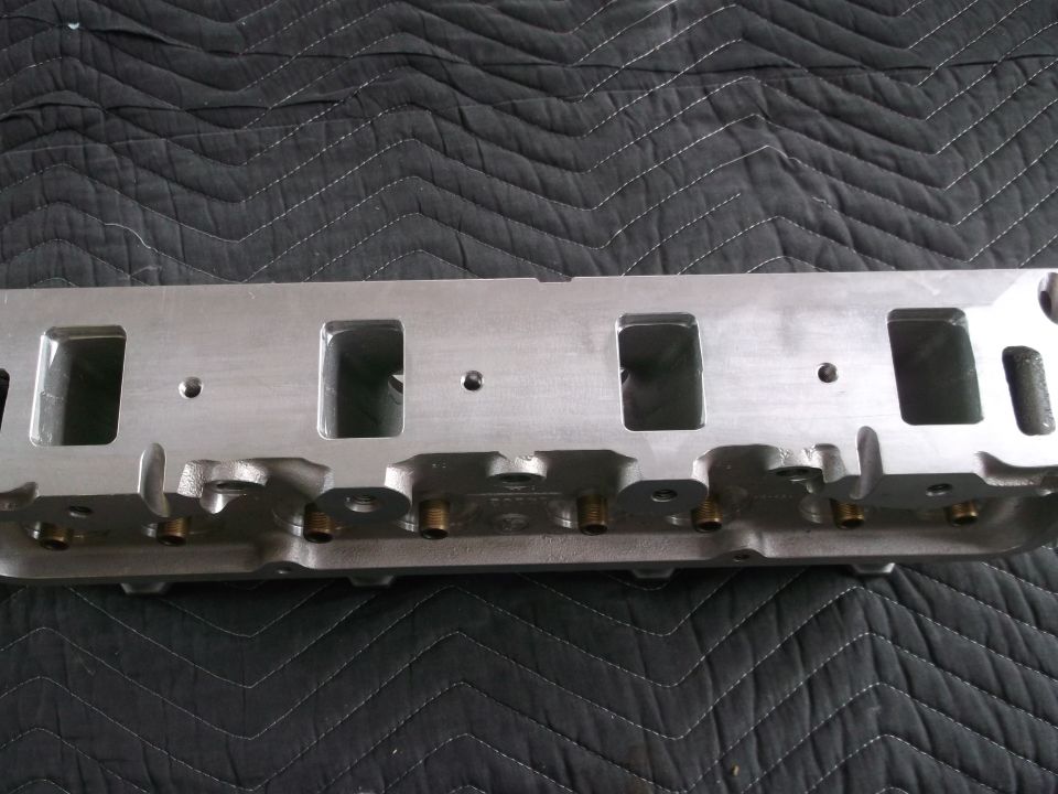 Aluminum engine cylinder head with rectangular intake ports, resting on a black quilted mat