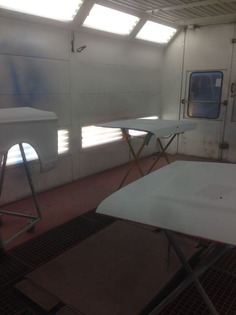 1964 Ford Fairlane - Automotive parts are prepared for painting inside a well-lit spray booth.