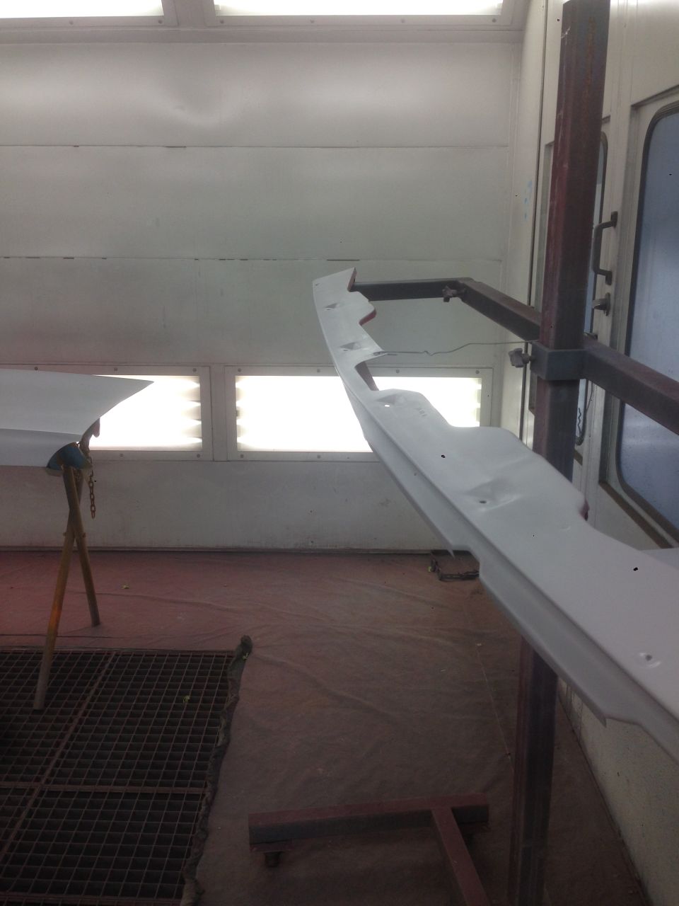 White car bumper or trim piece on a stand inside a spray booth