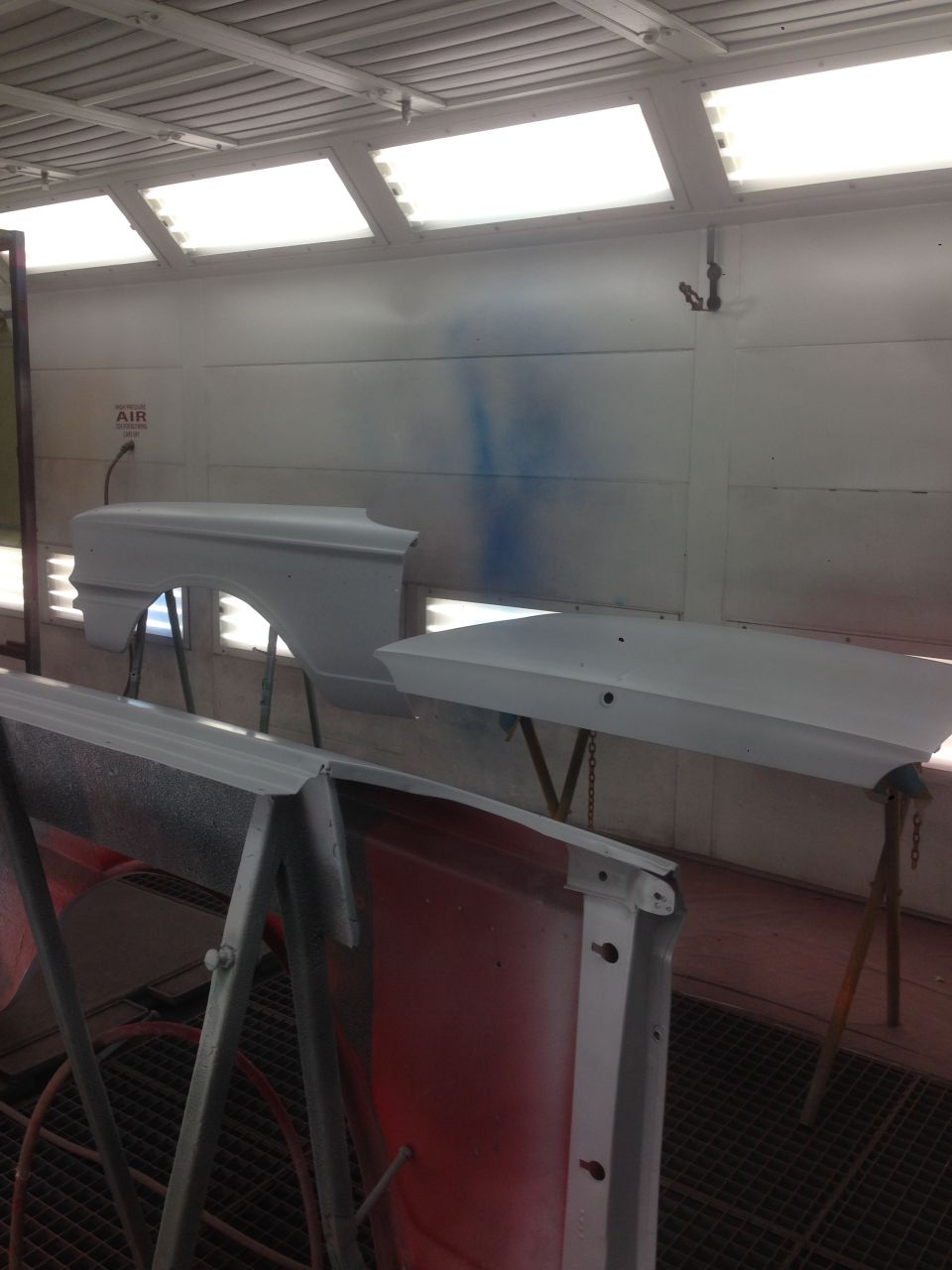 Car fender and hood, primed white, in a paint booth