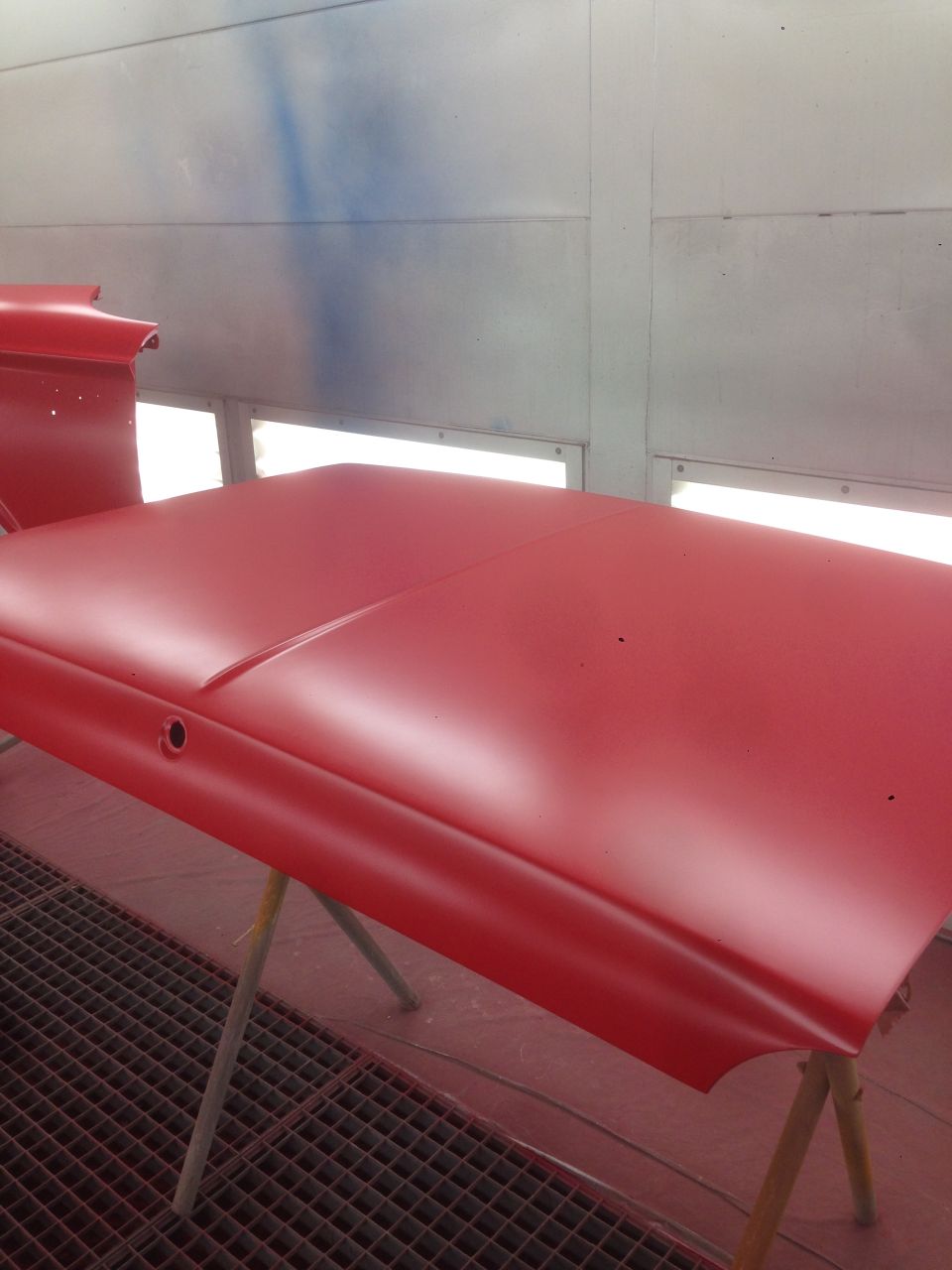 Red car hood on sawhorses in a spray booth, being prepped for paint