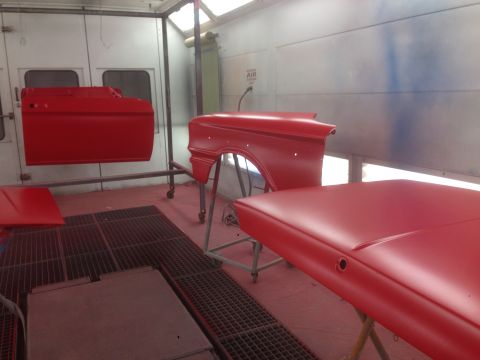 1964 Ford Fairlane - Car parts are being painted red inside a spray booth.