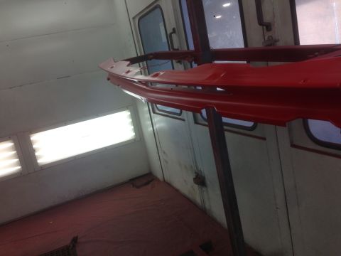 1964 Ford Fairlane - A red car bumper is suspended in a paint booth, ready for finishing.
