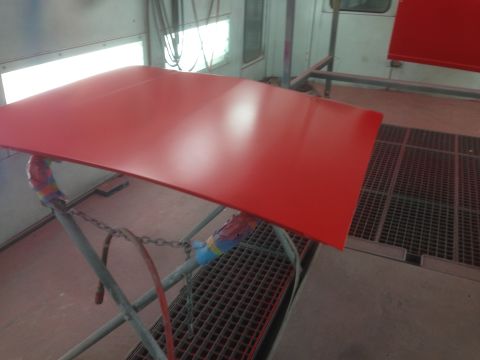 1964 Ford Fairlane - A red car hood is being prepped for painting in a booth.