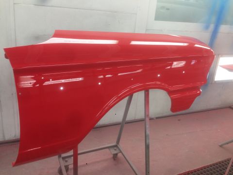 1964 Ford Fairlane - A freshly painted red fender is displayed on a stand inside a paint booth, awaiting reassembly.