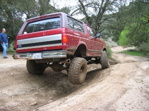 1989 Ford Bronco - This red 1989 Ford Bronco navigates a muddy off-road trail, showing its rear profile.