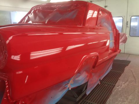 1964 Ford Fairlane - A bright red 1964 Ford Fairlane is being prepped for paint in a booth, showing its distinctive body lines.