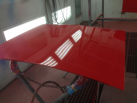 1964 Ford Fairlane - A freshly painted red car hood rests on sawhorses in a paint booth.