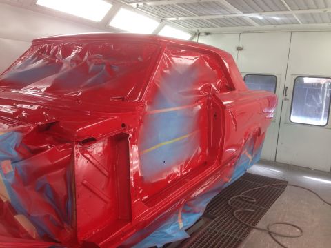1964 Ford Fairlane - A car body is being prepped and painted red inside a professional paint booth.