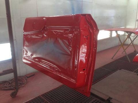 1964 Ford Fairlane - A red car door is being painted in a spray booth, with other car parts visible in the background.