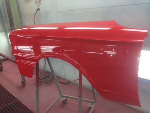 1964 Ford Fairlane - A red car fender is mounted on a stand, likely in a paint booth for refinishing.