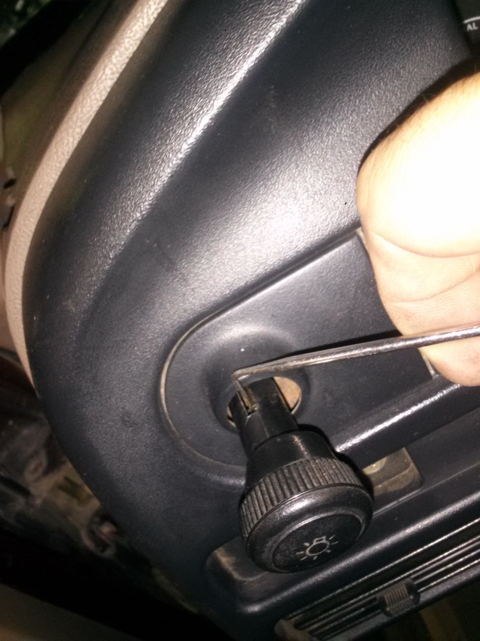 Hand using a tool to adjust a knob on a vehicle's dashboard