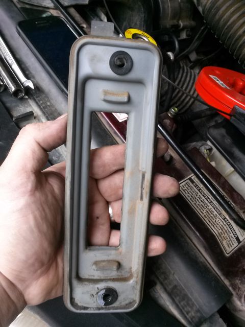 1996 Ford Bronco - A hand holds a gray metal bracket with a rubber grommet, against a backdrop of engine components.