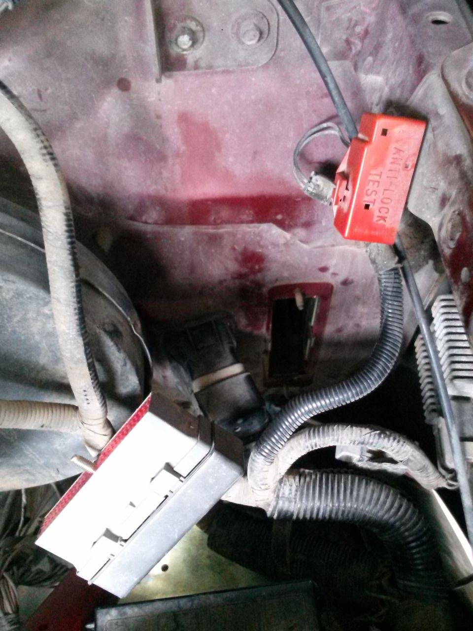 Close-up of engine bay wiring, including a red ABS test connector and a fuse box