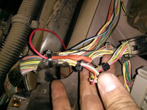 1996 Ford Bronco - A person's hands are shown manipulating a complex vehicle wiring harness with many colored wires and connectors.