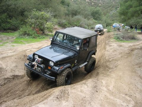 1989 Ford Bronco - A group of off-road vehicles navigates a challenging dirt path in a wooded area.
