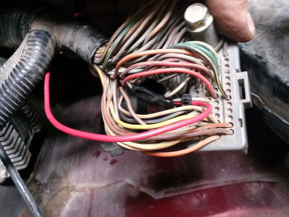 Engine wiring harness with red, yellow, and green wires connected to a gray connector. A hand is visible