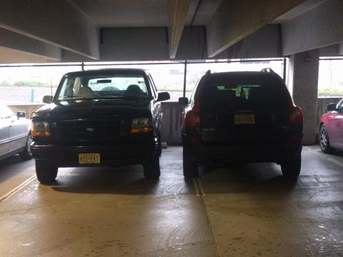 1995 Ford Bronco - Two SUVs are parked side-by-side in a covered parking structure, with a pink car visible to the right.