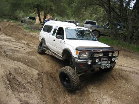 1989 Ford Bronco - This modified Toyota Tacoma navigates a challenging dirt path, with other vehicles present in the wooded area.