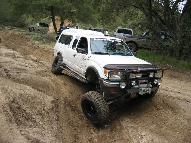 White lifted Toyota Tacoma with camper shell and winch bumper on a dirt trail