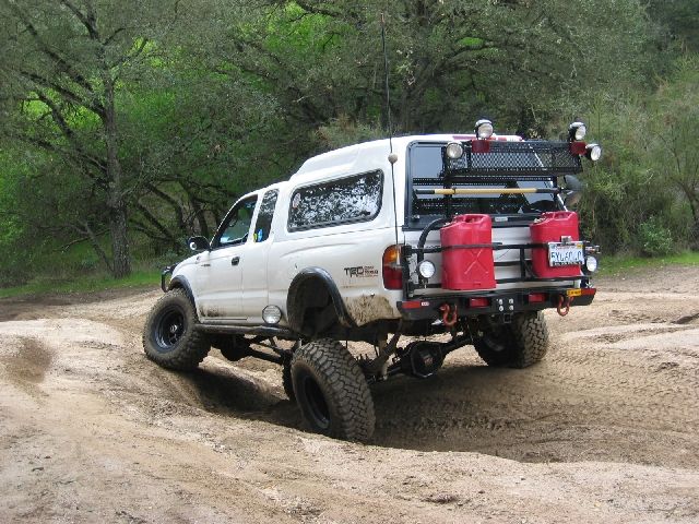 White Toyota Tacoma with shell, jerry cans and light bar flexing on a dirt trail