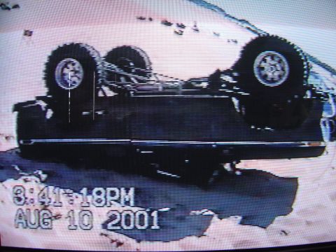 1978 Ford Bronco - A black SUV is seen overturned on its side, with its wheels and undercarriage exposed. The timestamp indicates August 10, 2001.