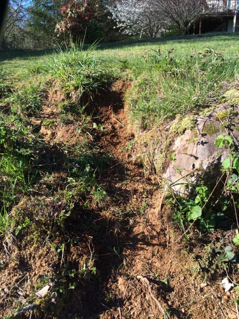 1989 Ford Bronco - A section of a grassy hillside has eroded, revealing exposed dirt and a large rock formation.