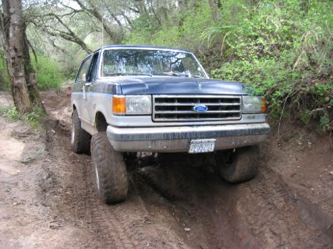 1989 Ford Bronco - Ford Bronco navigating a challenging dirt path with steep inclines and muddy terrain.