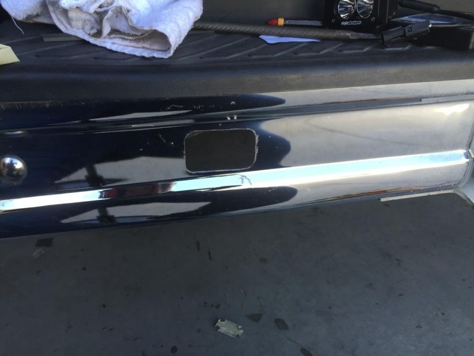Chrome rear bumper with a rectangular hole cut out. A towel and some tools are on the truck bed above