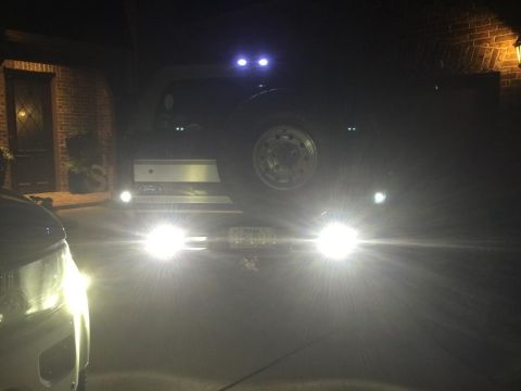 1996 Ford Bronco - The rear of a Ford truck is illuminated by its bright headlights at night, with a spare tire visible.